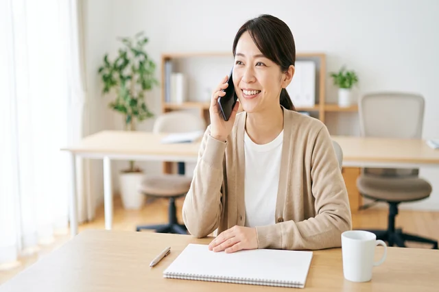 事務所でスマートフォンの通話に応対する女性スタッフ